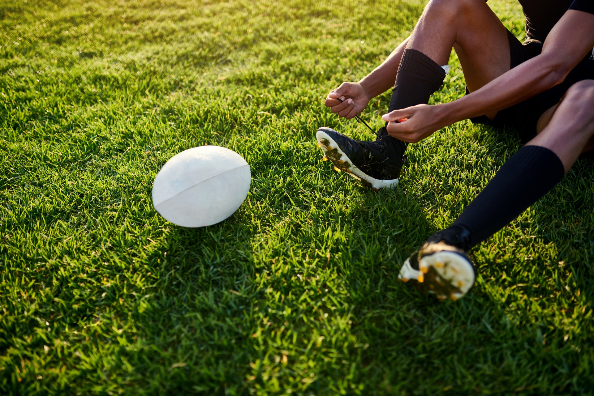 Abgeschnittener Schuss eines nicht wiederzuerkennenden Sportlers, der allein sitzt und seine Schnürsenkel bindet, bevor er tagsüber Rugby spielt